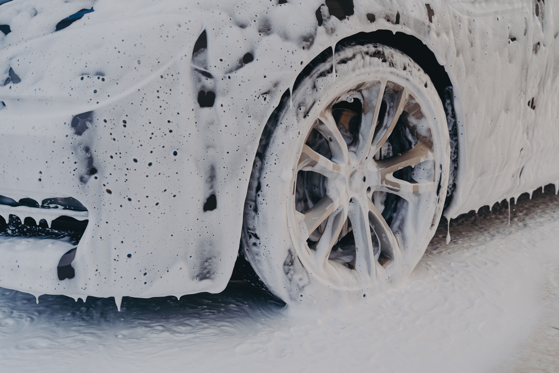 Car wheel in white soap foam at carwashing service station