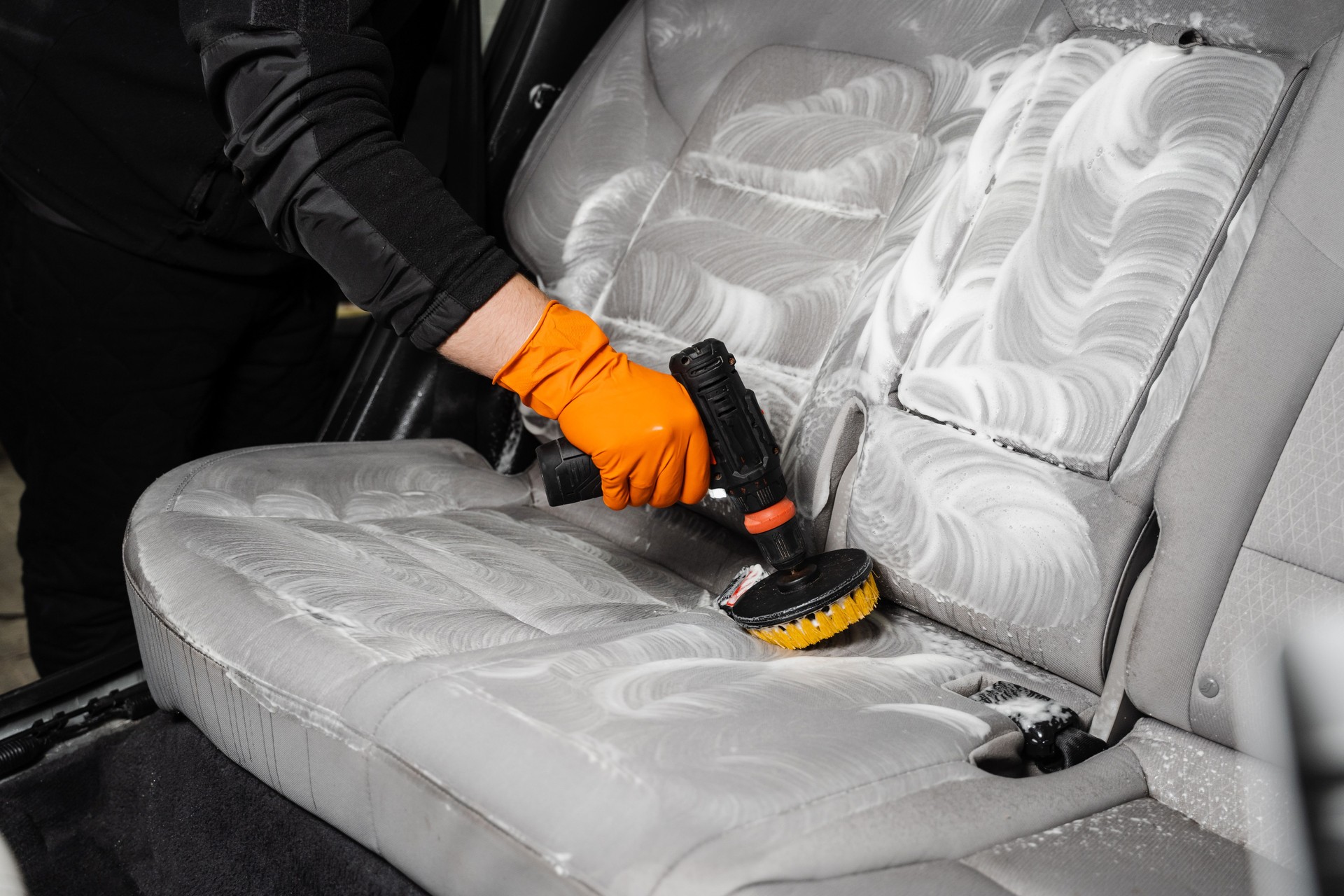 Smearing detergent on car textile seats using drill with brush for dry cleaning. Applying detergent on textile seat in car interior for dry cleaning.